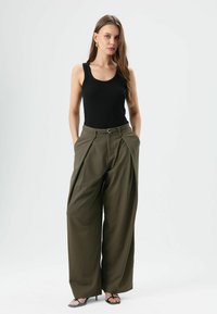 Zwart geribd tanktopje gecombineerd met olijfgroene wijde broek met ceintuurriem en voorplooien, tegen een neutrale achtergrond.