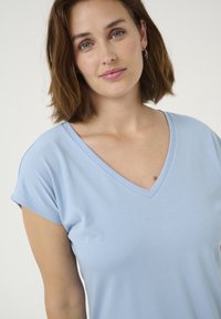 T-shirt bleu clair à col V et manches courtes, fabriqué en tissu doux. Présente une texture lisse et une coupe décontractée.