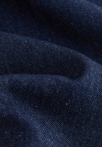 Dunkelblauer Denimstoff mit sichtbarer Köperbindung und leichten Falten, die Schatten und Textur erzeugen.