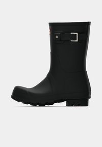 Botte de pluie en caoutchouc noir à bout arrondi, avec une semelle texturée et une boucle réglable sur le côté. Fini lisse et hauteur cheville.