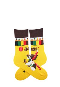 Żółte skarpetki z niedźwiedziem trzymającym pędzel, ozdobione kolorowymi ołówkami na górze oraz czerwoną okrągłą aplikacją z napisem "12."