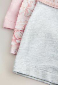 Trois pièces de tissu pliées en rose, motif floral rose et gris clair, montrant les détails de l'ourlet et des coutures.