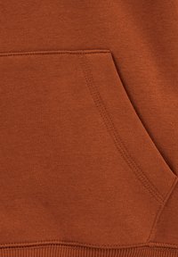Tessuto di felpa color ruggine con tasca a marsupio, orlo a coste e una texture morbida, con dettagli in cucitura lungo la tasca e le cuciture.