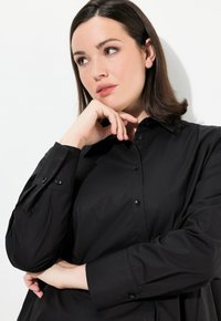Camicia nera con colletto, caratterizzata da maniche lunghe e bottoni neri a contrasto, realizzata in un tessuto liscio.
