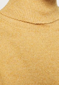 Tissu tricoté jaune avec texture côtelée et col roulé plié en gros plan.