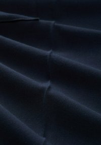 Dunkelblauer Stoff gefaltet mit sichtbarer, weicher Textur und sanften Falten bei schwachem Licht.