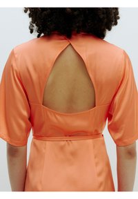 Oranje satijnen jurk met korte, brede mouwen en een groot keyhole-detail aan de achterkant. Gladde textuur met een getailleerde taille en naadaccenten.