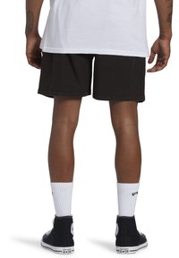 Pantalones cortos de mezclilla negra, ajuste relajado, con dobladillo estándar. Se llevan con calcetas blancas y zapatillas altas negras. Tatuaje visible en la pierna izquierda.