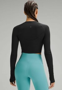 Schwarzes, kurzes Langarmoberteil und türkisfarbene High-Waist-Leggings. Das Oberteil hat eine glatte Textur und eine taillierte Passform, mit Logo-Detail.