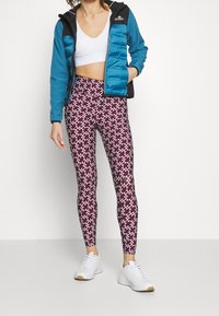 Blue and black zip-up jacket over a white crop top, paired with multicolored patterned leggings and white shoes.