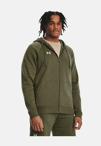 Olivgrüne Zip-Hoodie aus weichem, strukturiertem Stoff mit einer frontalen Tasche, verstellbarem Kordelzug an der Kapuze und Logo-Akzent auf der Brust.