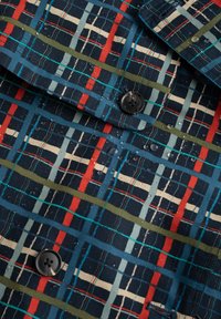 Camicia a fantasia con una base blu navy scuro e linee a griglia rosse, verdi, azzurro chiaro e crema. Tessuto testurizzato con gocce d'acqua visibili.