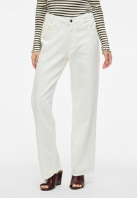 Vaqueros anchos blancos de denim con una textura suave. Cuenta con bolsillos delanteros y un cierre con un solo botón. Combinados con una blusa a rayas.