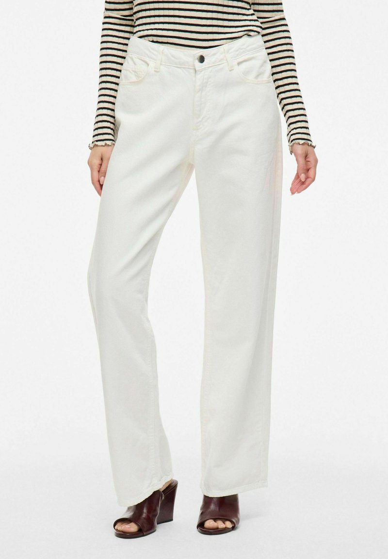 Vaqueros anchos blancos de denim con una textura suave. Cuenta con bolsillos delanteros y un cierre con un solo botón. Combinados con una blusa a rayas.