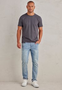 Šedé tričko s kulatým výstřihem, v kombinaci se světle modrými džíny a bílými teniskami. Oblečení má uvolněný, pohodlný střih.