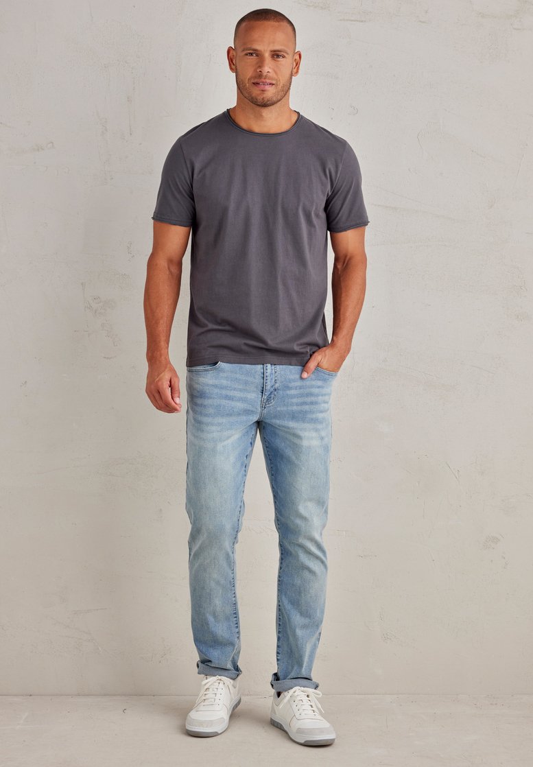 Šedé tričko s kulatým výstřihem, v kombinaci se světle modrými džíny a bílými teniskami. Oblečení má uvolněný, pohodlný střih.