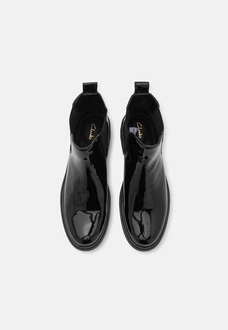 Botas de tobillo de charol negro con paneles elásticos a los lados, punta redonda y tiradores para facilitar el uso. Superficie lisa y brillante con un diseño minimalista.