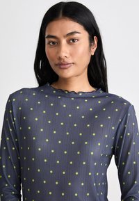 Maglietta a maniche lunghe blu navy in tessuto testurizzato. Caratterizzata da pois verdi e un colletto scallop. Vestibilità slim con sottili righe orizzontali.