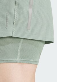 Svijetlozelena aktivna odjeća s teksturiranim, mrežastim uzorkom. Dizajn uključuje reflektirajuće akcente i prilagođene unutarnje kratke hlače.