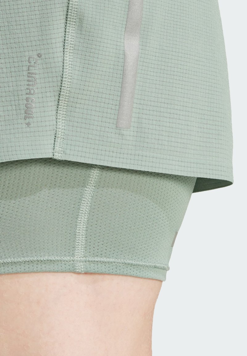 Hellgrüße Sportbekleidung mit einem strukturierten Rastermuster. Das Design umfasst reflektierende Akzente und einen figurbetonten Innenshort.