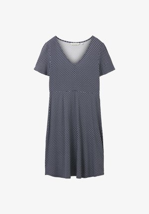 Femme portant une robe à manches courtes, longueur genoux, à motif noir et blanc, avec des chaussettes blanches et des baskets blanches, debout, bras détendus.
