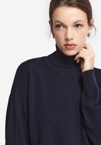 Marinblå polotröja med ribbade ärmslut och halsringning, mjuk stickad textur, lös passform och med sänkt axelsömn för en avslappnad stil.
