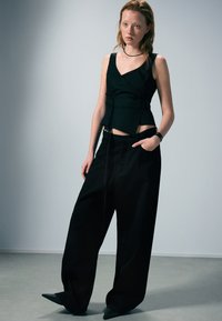 Haut noir sans manches avec un design portefeuille, associé à un pantalon noir à jambes larges. L'ensemble présente une silhouette épurée et une texture lisse.