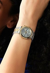 Orologio da polso con bracciale in metallo argento e oro, quadrante blu chiaro, tre sottocifre cronografo, dettagli oro e lunetta testurizzata.