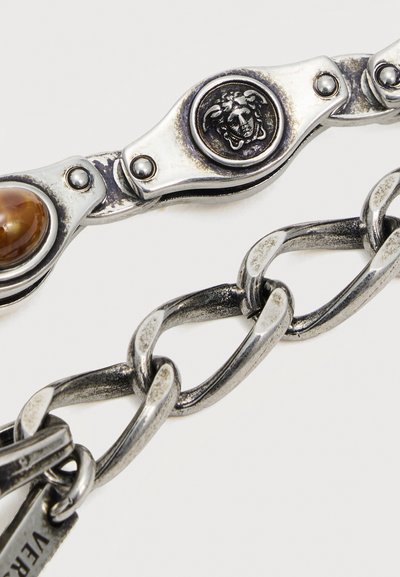 Bracelet chaîne en argent avec des maillons ovales, orné d'un emblème tête de Méduse et d'une pierre marron sertie dans un décor métallique.