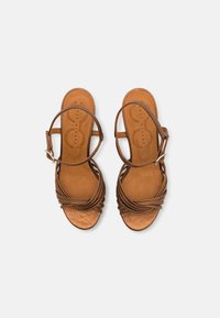 Brown leather sandals with a braided strap design, open toe, and ankle buckle. Flat, smooth sole with a cushioned footbed.