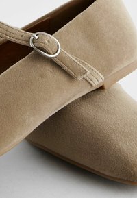 Beige suède kingad, mille otsaga, hõbese ringikujulise pandlaga ja sileda tekstuuriga pinnaga. Nähtav kummist põhi.