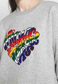 Felpa grigia con ricamo a cuore multicolore e testurizzato, con la scritta "Michael Kors" in caratteri in grassetto e giocosi.