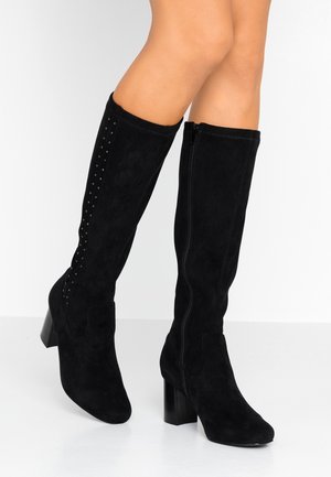 Bottes femme en daim noir montantes jusqu’au genou, avec talons blocs, fermeture éclair latérale et petits clous décoratifs sur les côtés extérieurs.