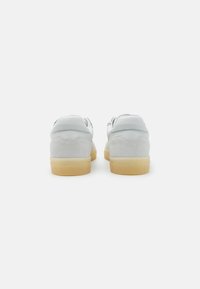 Sneakers bianchi in pelle e suede con suola in gomma, caratterizzati da un esterno liscio e un design con retro arrotondato. Nessun marchio visibile.