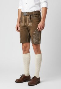 Bruna läderhosen med blommig broderi, bältesslingor, framfickor och sidoknappar. Bärs med krämfärgade knästrumpor och bruna skor.