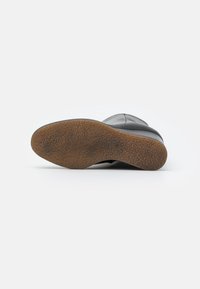Suela de bota de cuero negro con una superficie texturizada, que presenta una suela de goma marrón y una forma curvada para mejorar el agarre y la durabilidad.