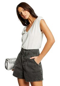 Shorts de mezclilla gris de tiro alto con bolsillos frontales, combinados con una camiseta blanca ajustada de cuello en V. Se sostiene un clutch metálico plateado en una mano.