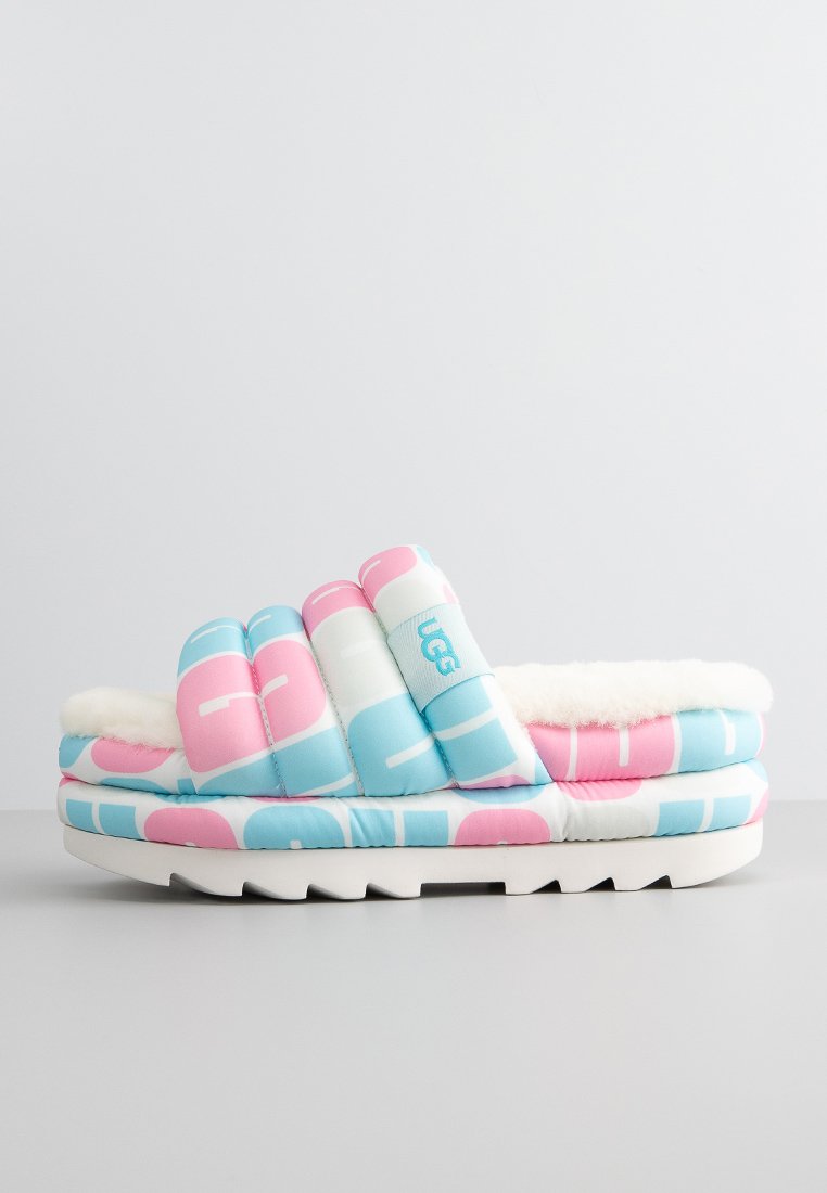 Pantofole UGG multicolori con un design imbottito blu, rosa e bianco, un interno morbido e peloso e una suola spessa bianca.