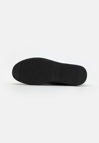 Black shoe sole with a textured, ribbed pattern. Durable rubber material with embossed branding. Flat design for stability and traction.