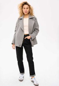 Szary wełniany płaszcz z podwójnym zapięciem i klapami, z przednimi kieszeniami, w połączeniu z czarnymi dżinsami i białymi trampkami z szarymi akcentami.