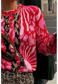 Cárdigan de punto con vibrantes patrones florales en rojo, rosa y negro, con dos botones rosas y un acabado texturizado. Combínalo con accesorios estampados.