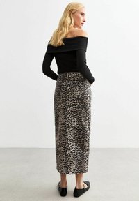 Svart avskuren topp med leopardmönstrad kjol, som har en snygg lång form, kontrasterande texturer och sidfickor; kombinerat med svarta ballerina-skor.