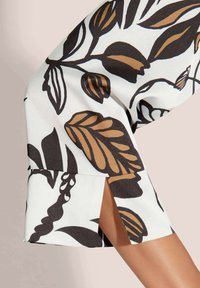 Blumenkleid mit weißem Hintergrund und schwarzen sowie braunen Blattmustern, kurzen Ärmeln und seitlichen Schlitzen für eine moderne Silhouette.