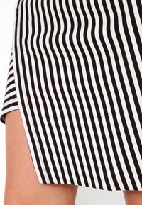 Tissu rayé noir et blanc avec des lignes ondulées alternatives, fait d'un matériau lisse. L'ourlet présente une courbe subtile et des coutures soignées.