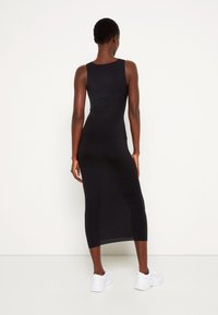 Schwarzes, figurbetontes, ärmelloses Midikleid mit gerader Silhouette. Getragen mit weißen Sneakers, aus glattem, dehnbarem Stoff.