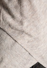 Pull en laine gris clair avec un tricot texturé, présentant une ourlet diagonal et une apparence douce, légèrement chinée.