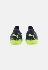 Navy blue soccer shoes with neon green accents, textured rear, and a cat logo. Features molded rubber outsole with traction studs.