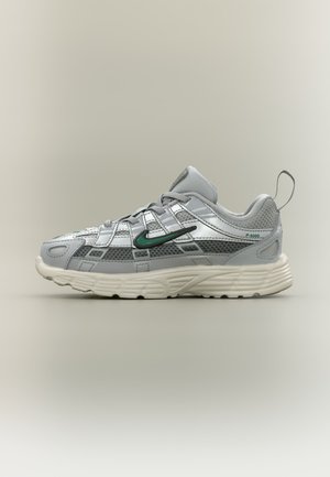 Szaro-biały sportowy but z zielonym znakiem Nike, szczegółami z siateczki, grubą podeszwą i pętlą do zakładania na gładkim neutralnym tle.