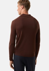 Brauner Strickpullover mit Kragen und langen Ärmeln, der eine taillierte Passform und gerippte Bündchen sowie Saum aufweist. Glatte Textur, minimale Details.