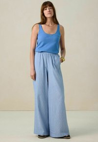 Débardeur bleu à encolure arrondie associ é à un pantalon large texturé bleu clair avec une taille élastique. Accent avec un bracelet en or simple.